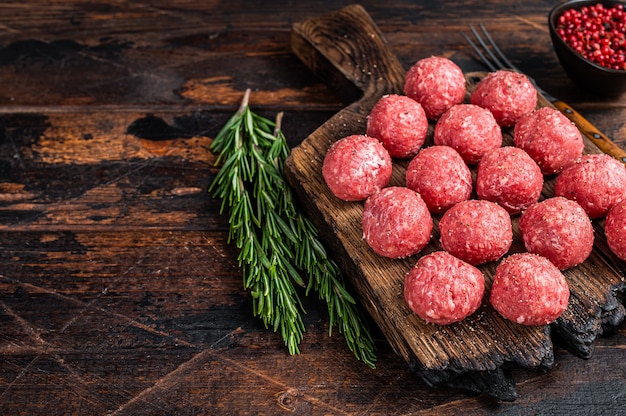 Boulettes de viande crues crues de boeuf haché et viande de porc au romarin. Fond en bois foncé. Vue de dessus. Copiez l'espace.