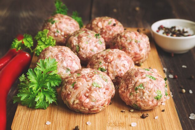 Boulettes de viande crues avec du persil et des piments sur une table en bois rustique.