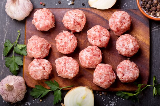 Boulettes de viande crues fraîches avec des légumes sur table sombre