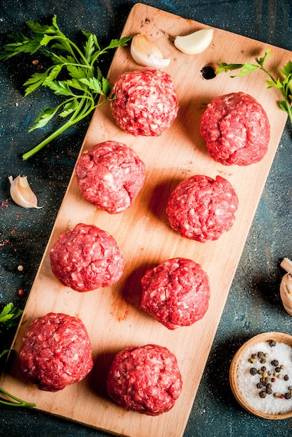 Boulettes de viande crues avec de l'huile d'olive et des épices sur une table en béton foncé, copyspace vue de dessus