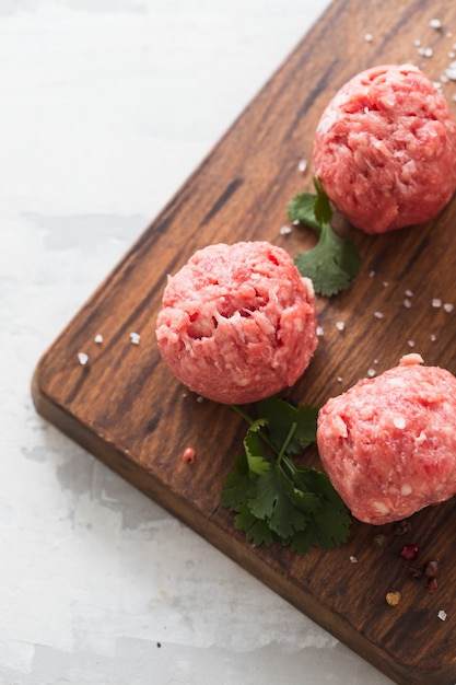 Boulettes de viande crues avec poivre et sel sur planche de bois