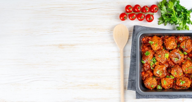 Boulettes de viande maison avec sauce tomate et épices servies dans une poêle noire sur fond de bois blanc