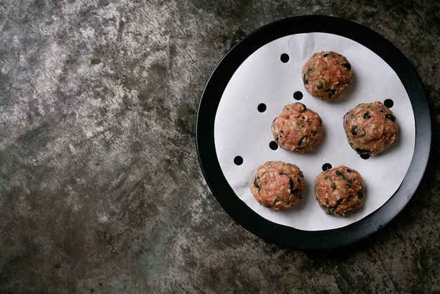 Boulettes de viande prêtes à cuire dans une assiette noire sur du papier sulfurisé. Mise à plat. Vue de dessus