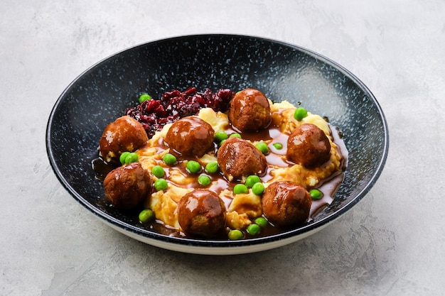 Boulettes de viande avec sauce servies avec purée de pommes de terre, pois verts et confiture de canneberges sur une assiette