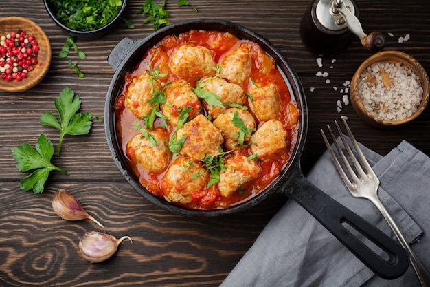 Boulettes de viande à la sauce tomate ail et persil dans une poêle en fer sur une surface en bois brun foncé