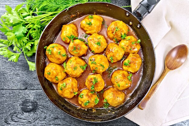 Boulettes de viande à la sauce tomate dans une poêle avec du persil, de l'aneth, une serviette et une cuillère sur un fond de planche de bois