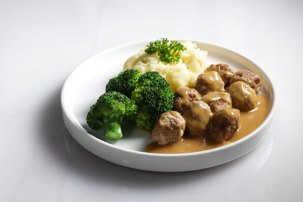 Boulettes de viande suédoises avec sauce brune aux champignons. Servi sur plaque en céramique, sur table blanche.