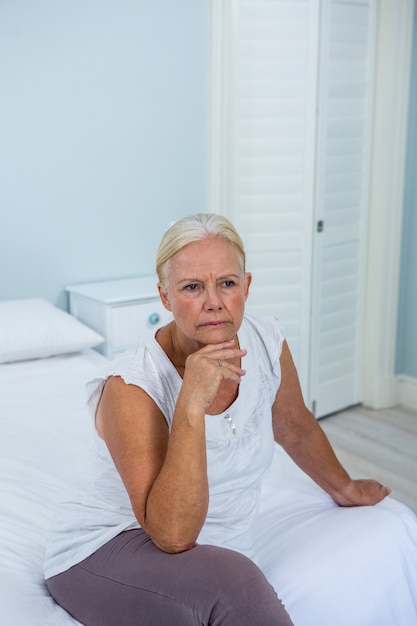 Bouleversé femme senior avec la main sur le menton assis sur le lit