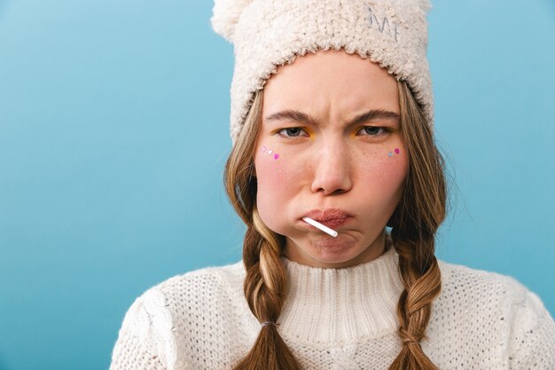 Bouleversé fille portant un chandail debout isolé, manger une sucette