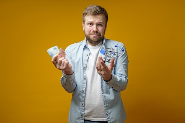 Bouleversé, l'homme barbu qui pleure tient dans les mains un caddie décoratif et de l'argent