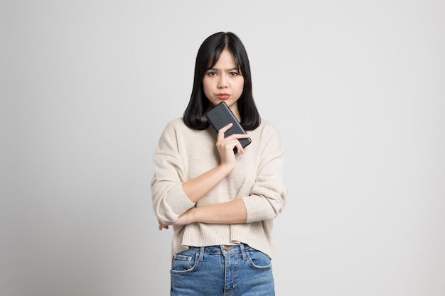 Bouleversé la jeune femme asiatique tenant un smartphone debout sur fond blanc isolé. Elle était très stressée et déprimée.