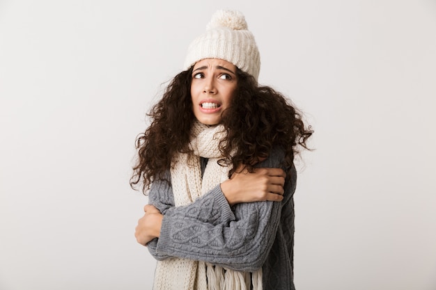 Bouleversé jeune femme portant un foulard d'hiver debout isolé sur un mur blanc, grelottant