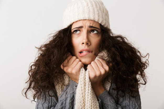 Bouleversé jeune femme portant un foulard d'hiver debout isolé sur un mur blanc, grelottant