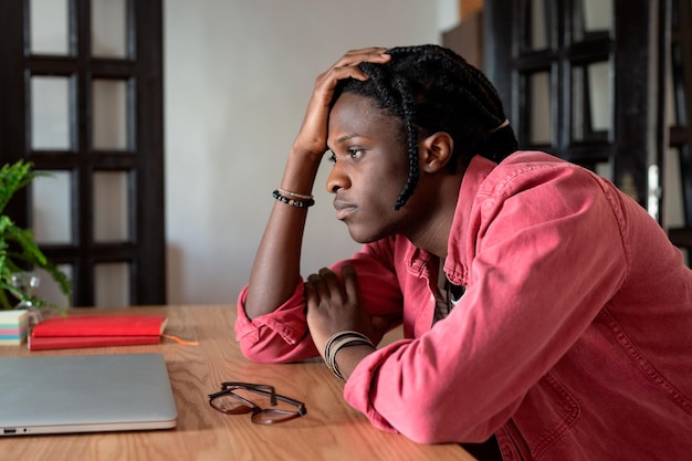 Bouleversé jeune homme africain travailleur à distance face à l'épuisement professionnel indépendant assis au bureau avec un ordinateur portable