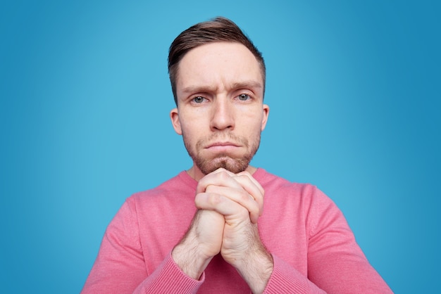 Bouleversé jeune homme en pull rose en gardant ses mains par le menton tout en pensant à quoi faire