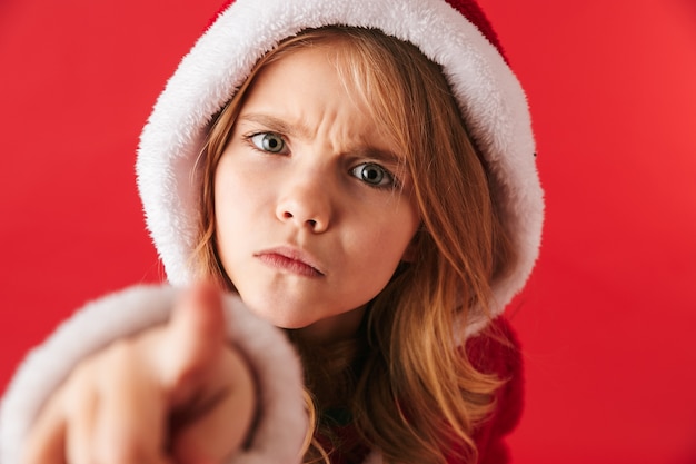 Bouleversé petite fille portant le costume de Noël debout isolé, pointant vers l'avant