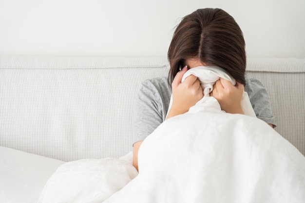 Bouleversé triste jeune femme brune assise dans son lit à la maison, avec copie espace