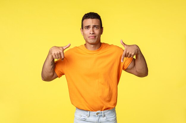 Bouleversé, triste mignon beau mec en t-shirt orange, pointant les doigts vers le bas