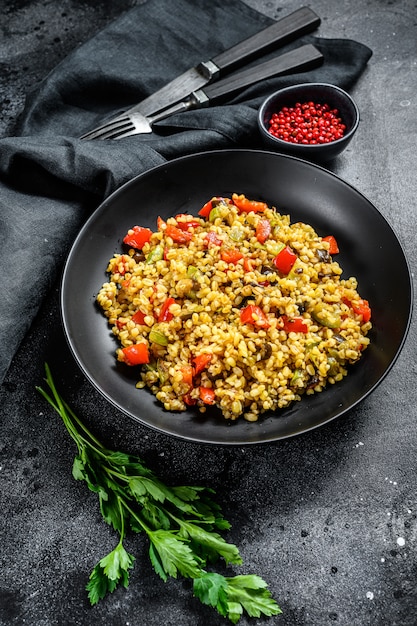 Boulgour avec légumes, oignons, poivrons, carottes et persil dans une assiette.