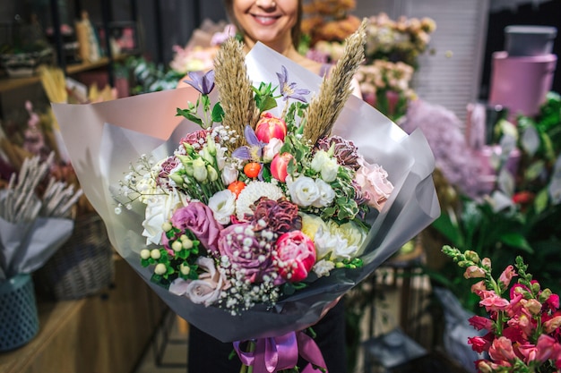 Bouqette sympa et colorée de fleurs différentes. Fleuriste femelle le tenir et sourire. Elle est dans un magasin de fleurs. Vue en coupe. Fermer.