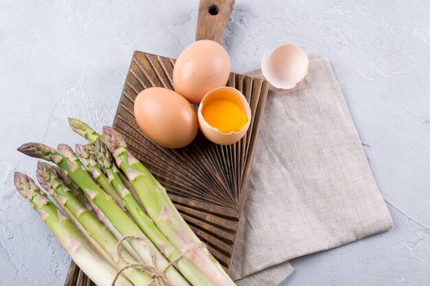 Bouquet d'asperges fraîches crues avec des œufs sur un fond de béton gris