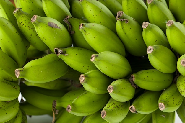 Bouquet de banane crue ou de banane verte placée sur une surface blanche avec un fond texturé gris en gros plan
