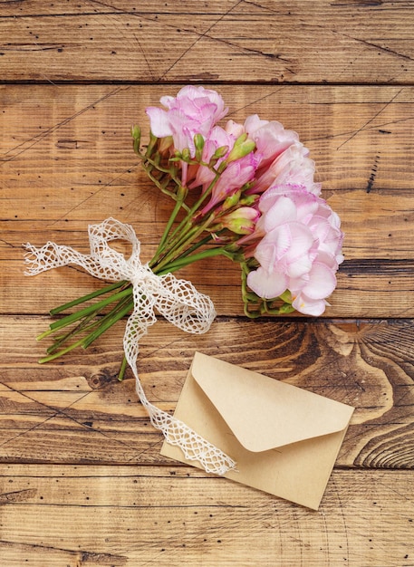 Bouquet de belles fleurs de freesia avec ruban et vue de dessus d'enveloppe. Maquette sur table en bois. Fleurs roses pour les fêtes, mise à plat. Anniversaire, fête des mères, concept de la Saint-Valentin