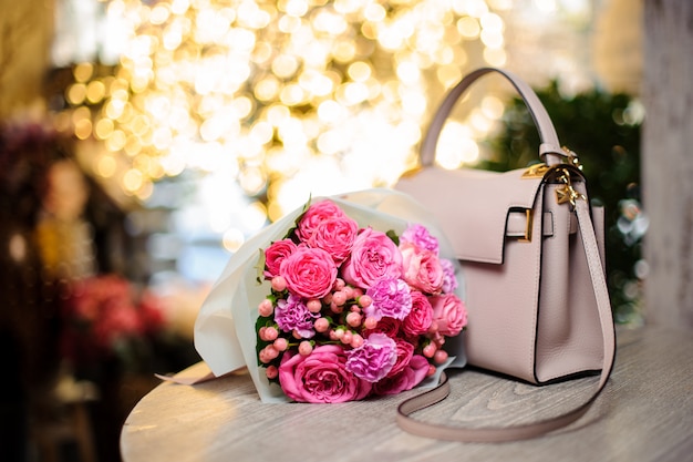 Bouquet de belles fleurs roses près du sac à main élégant sur la table