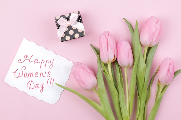 Un bouquet de belles fleurs de tulipes roses et une boîte-cadeau sur un fond rose à la mode texte de vacances de printemps bonne journée de la femme vue de dessus