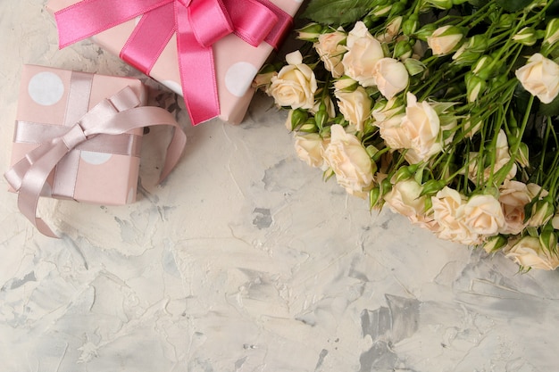 Un bouquet de belles mini roses tendres et une boîte cadeau sur un fond de béton clair