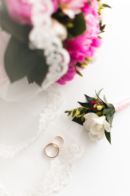 Bouquet de belles pivoines roses et alliances se trouvent sur une table blanche.