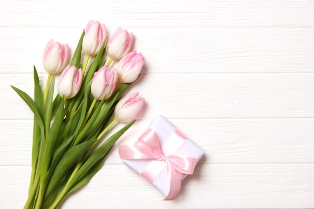 Un bouquet de belles tulipes et un cadeau sur une vue de dessus de fond en bois. Contexte de la fête des mères, Journée internationale de la femme. Vacances, offrez un cadeau. photo de haute qualité