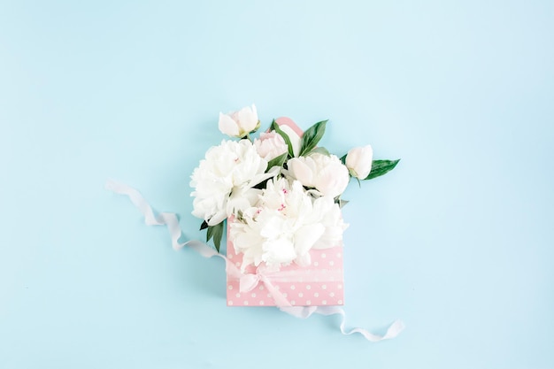 Bouquet blanc de pivoines dans une enveloppe pour fleurs sur fond bleu concept floral minimal greeti