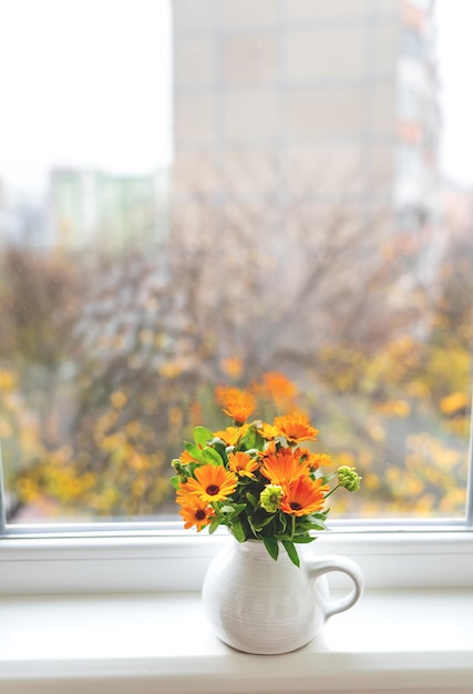 Un bouquet de calendula lumineux dans un vase à lait se dresse sur le rebord de la fenêtre automne lumineux avec une fenêtre