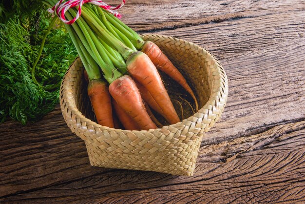 bouquet de carottes fraîches avec des feuilles vertes dans un panier en bois sur fond en bois