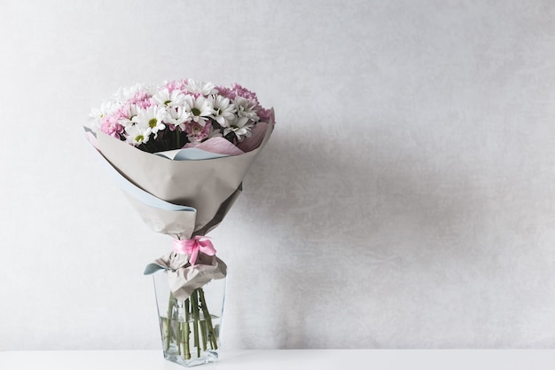 Bouquet de chrysanthèmes blancs et roses dans un vase en verre sur table.