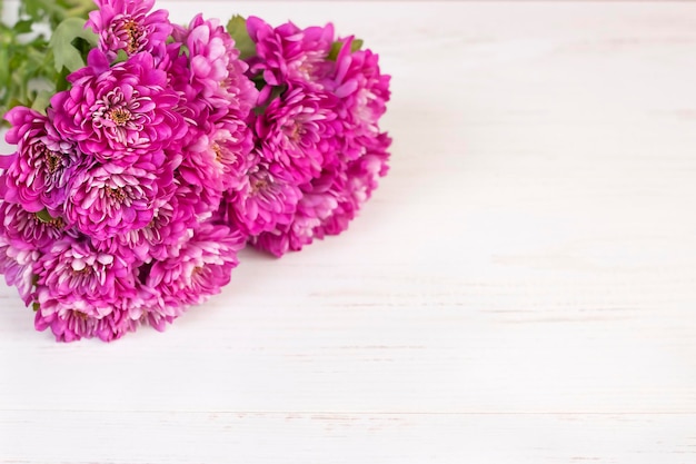 un bouquet de chrysanthèmes roses se trouve sur une surface en bois clair