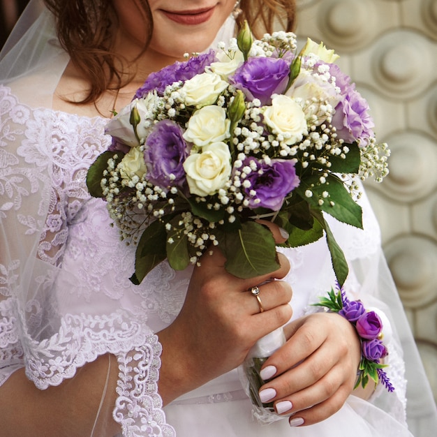 Bouquet délicat de roses blanches et violettes dans les mains du gros plan de la mariée