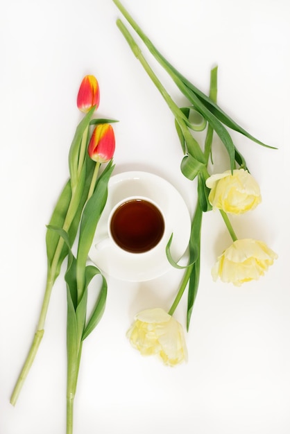 Un bouquet de délicates tulipes jaunes et une tasse de thé sur fond blanc Vue de dessus Le concept d'un blog ou d'un pigiste Carte de vœux de Pâques