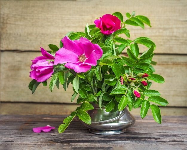 Un bouquet d'églantier rose foncé dans un vase en métal sur la table d'un gros plan de maison de campagne