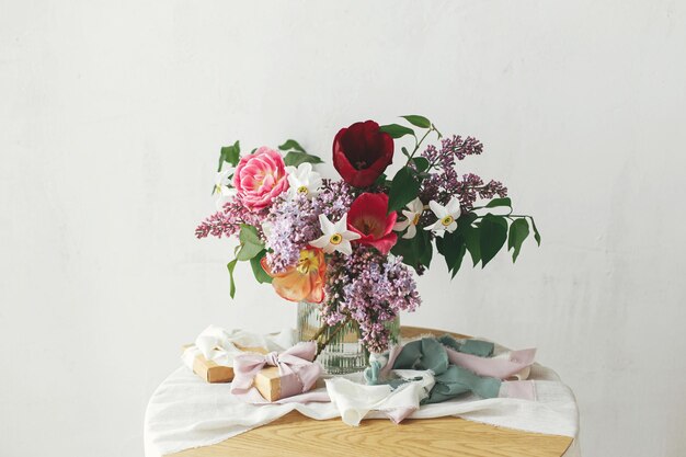 Bouquet élégant avec boîte-cadeau sur une table en bois rustique Bonne fête des mères Arrangement de jonquilles de tulipes lilas de printemps avec présent sur un tissu doux dans une chambre rustique moderne Bonne journée de la femme