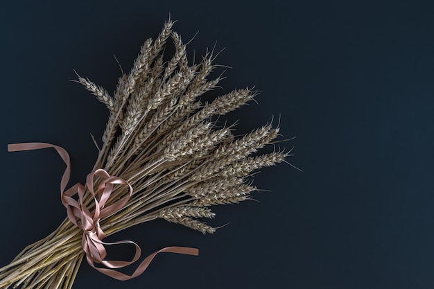 Un bouquet d'épis de blé attachés avec un ruban de satin sur fond sombre