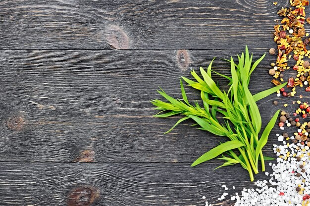 Bouquet d'estragon frais avec du sel, du poivre, des graines de fenugrec contre une planche de bois noire