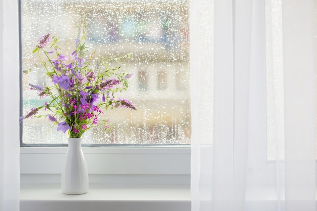 Bouquet d'été sur le rebord de la fenêtre blanche avec des gouttes de pluie