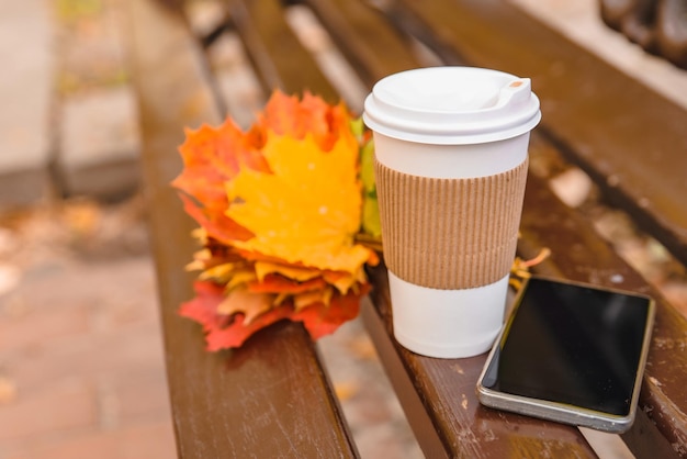 Bouquet de feuilles d'érable jaunes avec une tasse de café et un téléphone au banc du parc de la ville