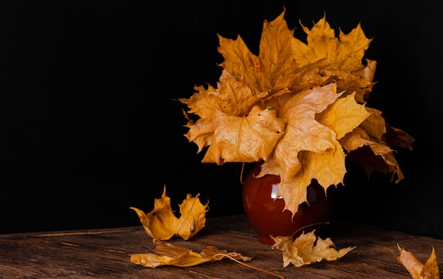 Bouquet de feuilles mortes d'automne dans un vase d'argile. Nature morte sur fond sombre.