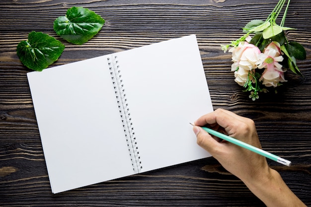 Bouquet de fleur avec main écrivant sur cahier journal vide cahier rustique en bois avec copie