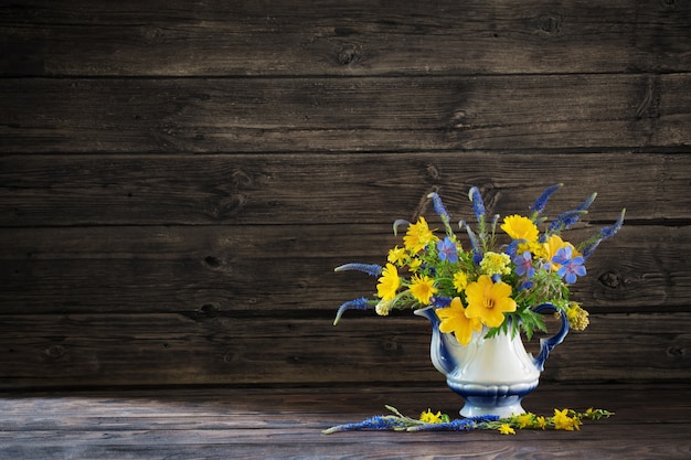 Bouquet de fleurs bleues et jaunes en théière sur table en bois