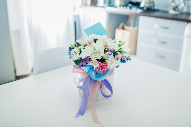 Bouquet de fleurs avec carte dans une boîte cadeau laissée dans la cuisine. Surprise pour femme. Présent pour les vacances
