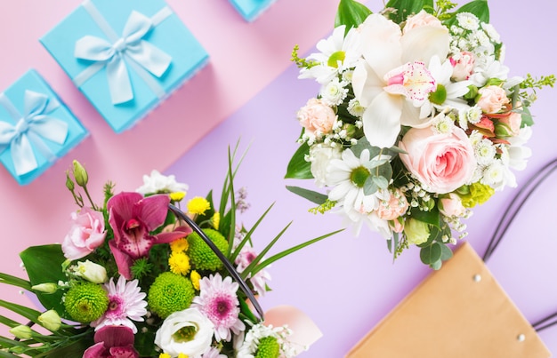 Bouquet de fleurs avec des coffrets cadeaux bleus sur fond coloré à plat vue de dessus